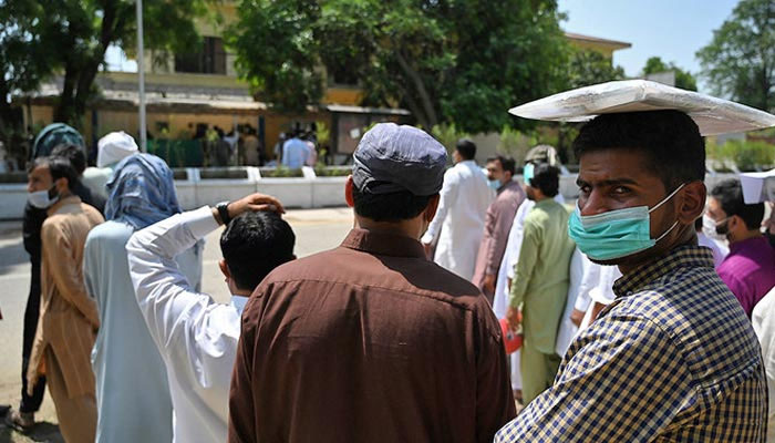 Citizens wearing face masks amid concerns over the spread of coronavirus, wait in a queue in Islamabad, Pakistan, on May 19, 2021. — AFP
