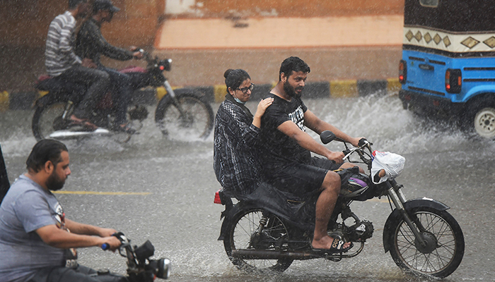 Commuters ride motorbikes along a street during a monsoon rainfall in Karachi on July 5, 2022. — AFP