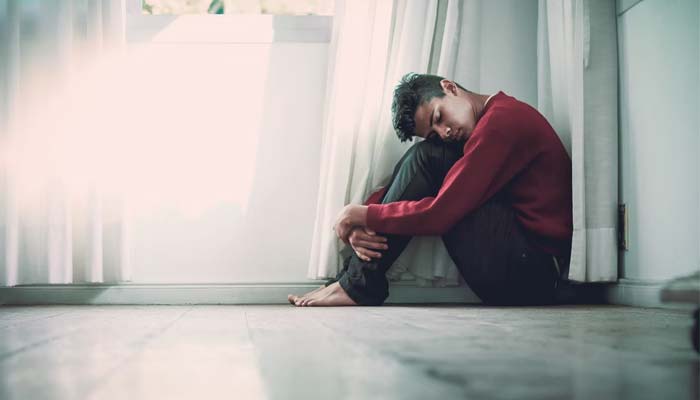 A boy sitting on the floor while he wraps his hands around his legs.— Unsplash