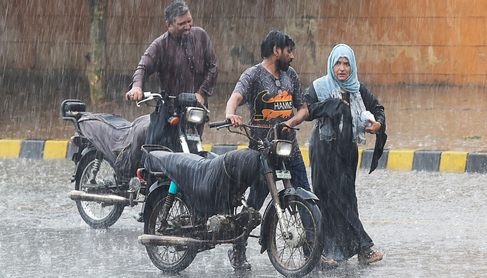 Commuters push their motorbikes along a street during a monsoon rainfall in Karachi on July 5, 2022. — AFP