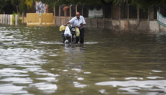A man pushes his motorbike along a flooded street after a monsoon rainfall in Karachi on July 9, 2022. — AFP