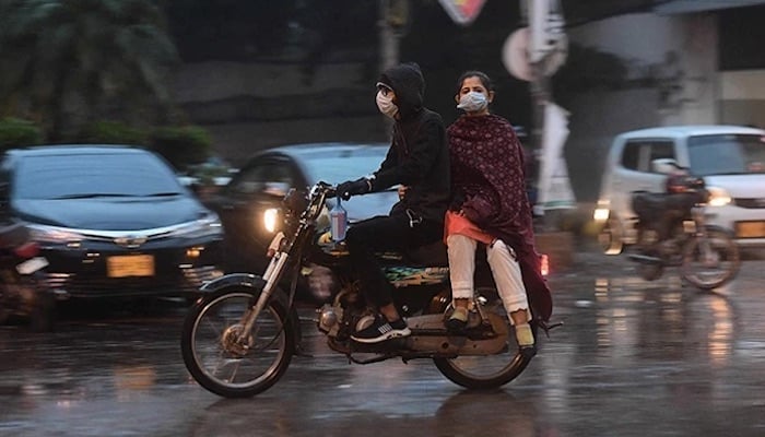 Commuters ride on a motorbike along a road during rainfall in Karachi. Photo: AFP