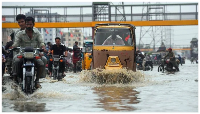 Commuters pass through a road flooded with rainwater in Karachi. — AFP/ File