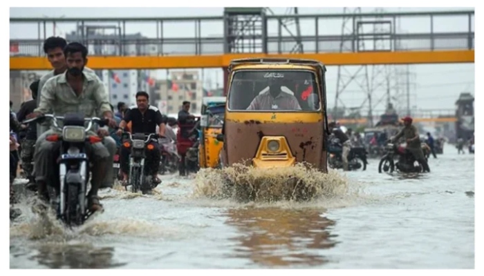 Commuters pass through a road flooded with rainwater in Karachi. — AFP/ File