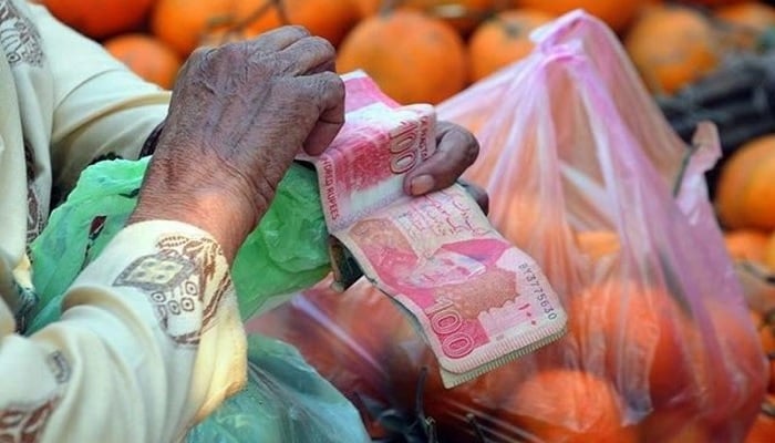 A file photo of a man in Pakistan sitting next to a bag of groceries and counting money. Photo: AFP