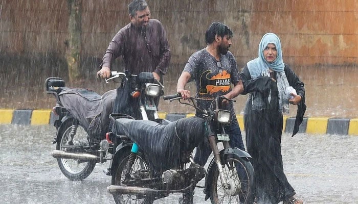 Commuters push their motorbikes along a street during a monsoon rainfall in Karachi on July 5, 2022. —AFP