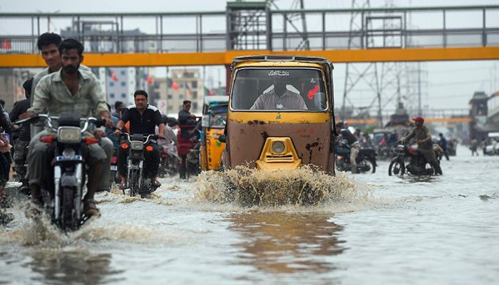 Commuters cross a flooded street during heavy monsoon rains in Karachi on Tuesday. — AFP