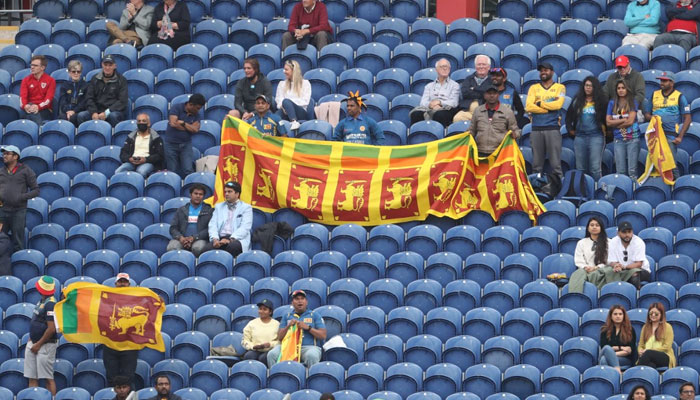 Sri Lankan cricket fans wave their countrys flags while sitting on the stands in a cricket stadium. — AFP/File