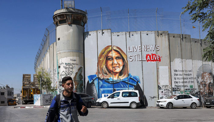 A youth walks past a mural depicting slain Al Jazeera journalist Shireen Abu Akleh, who was killed while covering an Israeli army raid in Jenin in May, drawn along Israels controversial separation barrier in the biblical city of Bethlehem in the occupied West Bank on July 6, 2022. — AFP