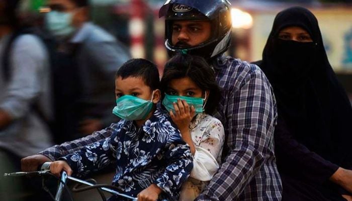 A family riding on a bike wear facemasks as a precaution against the coronavirus on October 29 in Karachi, — AFP