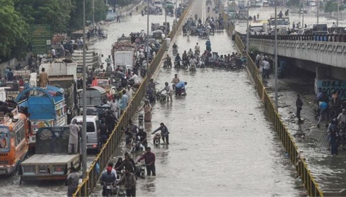 Commuters cross a flooded street after heavy rainfall in Karachi. — AFP