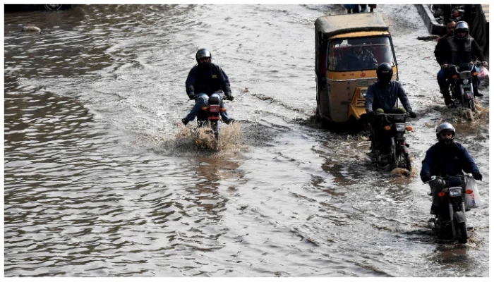 Motorcyclists and a rickshaw pass through rainwater filled on road in Karachi. — AFP/File