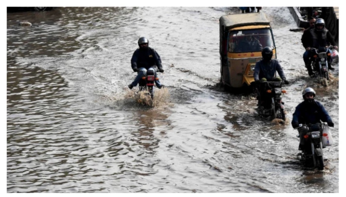 Motorcyclists and a rickshaw pass through rainwater filled on road in Karachi. — AFP/File