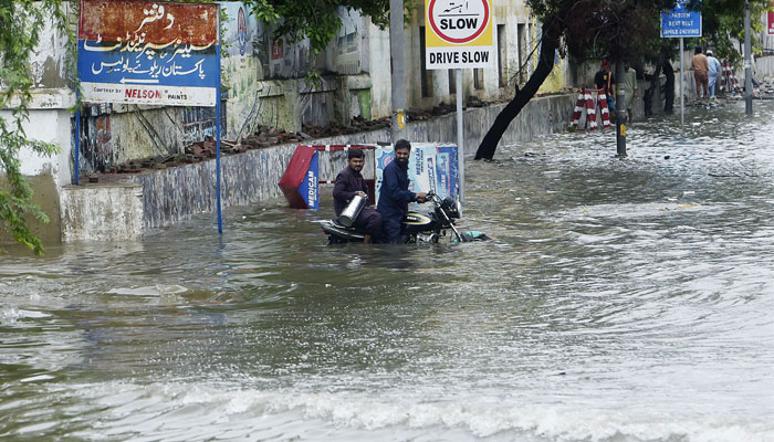 Motorcyclists wade through a flooded II Chundrigar Road after heavy rain .—  APP/File