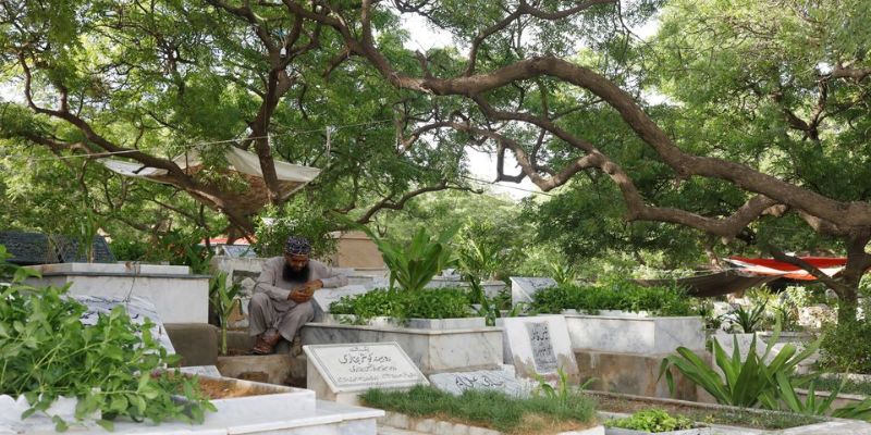 کراچی، پاکستان میں 12 جولائی، 2022 کو ایک شخص سخی حسن قبرستان میں بیٹھا فون پر دعا پڑھ رہا ہے، جو مرنے والوں کے رشتہ داروں کے بیجوں سے بھرا ہوا ہے۔ کراچی ایک وسیع و عریض بندرگاہی شہر ہے، جہاں 17 ملین آبادی سڑکوں اور عمارتوں کی خراب توسیع کا مطلب ہے کہ درختوں اور پارک لینڈ کے لیے جگہ کم اور کم ہے۔  رائٹرز