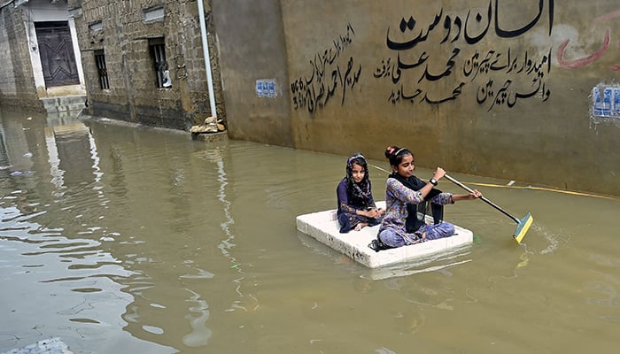 Girls use a temporary raft across a flooded street in a residential area after heavy monsoon rains in Karachi on July 26, 2022. — AFP