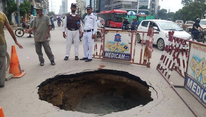 Police personnel stand around a sinkhole that has been formed at the Shaheen Complex Chowk roundabout in Karachi, on July 30, 2022. — Photo by author