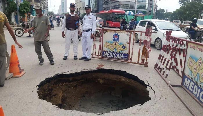 Police personnel stand around a sinkhole that has been formed at the Shaheen Complex Chowk roundabout in Karachi, on July 30, 2022. — Afzal Nadeem Dogar