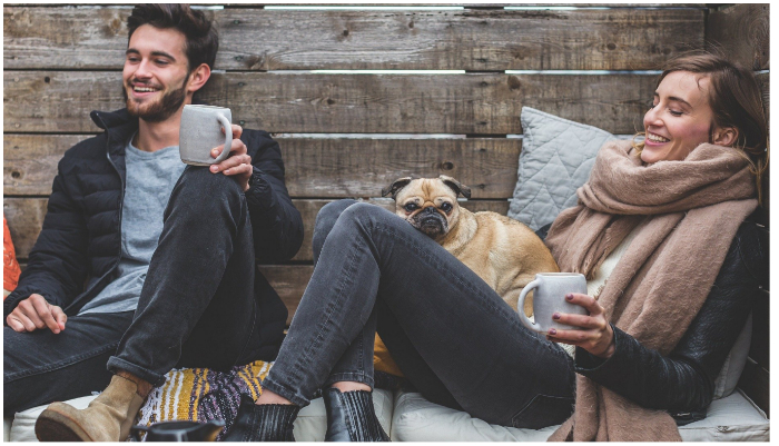 Representational image of a man and a woman sitting together with their dog and holding mugs in their hands. — Pixabay/ 5688709