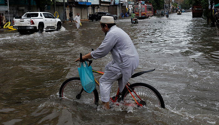 Seorang pria mengendarai sepeda di sepanjang jalan yang banjir, menyusul hujan lebat selama musim hujan di Karachi, Pakistan, 25 Juli 2022. — Reuters