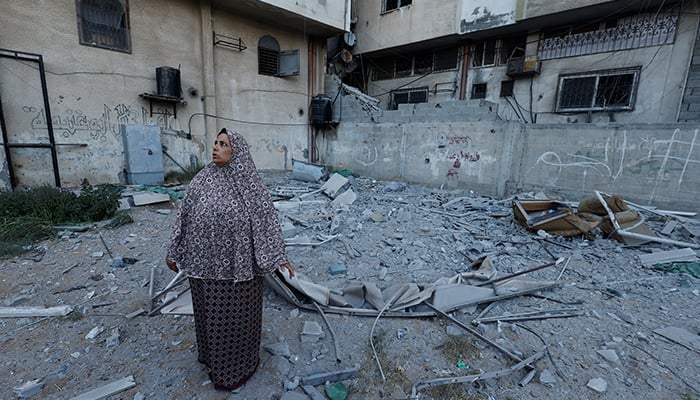 6 اگست 2022 کو غزہ شہر میں ایک خاتون تباہ شدہ عمارت کے پاس کھڑی دیکھ رہی ہے جہاں اسلامی جہاد گروپ کا سینئر کمانڈر تیسیر الجابری اسرائیلی حملوں میں مارا گیا تھا۔