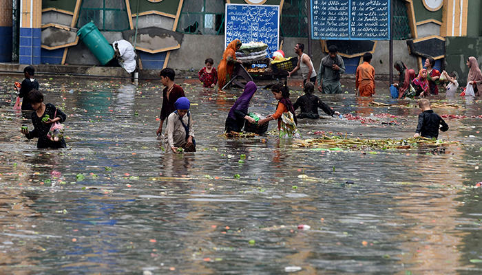 Orang-orang memetik sayuran dari air di pasar yang banjir setelah hujan deras di Lahore pada 21 Juli 2022. — AFP