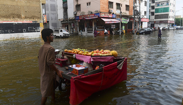 A fruit vendor pushes his cart across a flooded street following heavy monsoon rains in Karachi on July 26, 2022. A weather emergency was declared in Karachi as heavier-than-usual monsoon rains continue to lash Pakistans biggest city, flooding homes and making streets impassable. — AFP