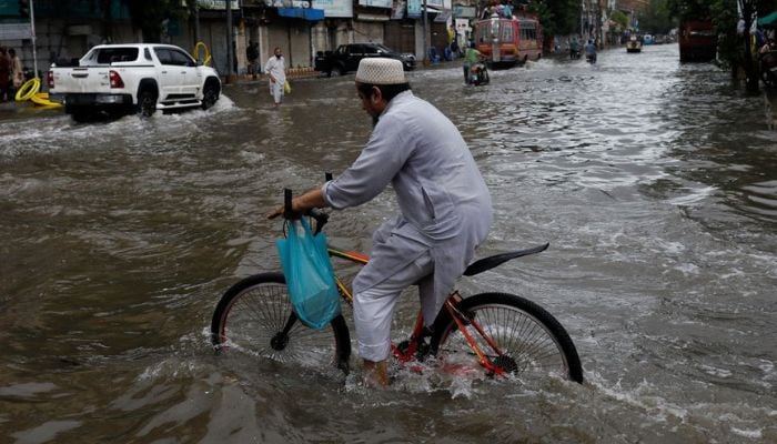 A man rides his bicycle along a flooded road, following heavy rains during the monsoon season in Karachi, Pakistan on July 25, 2022 — Reuters