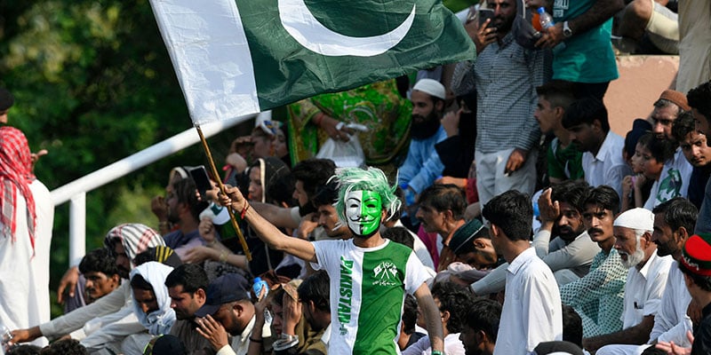 An enthusiast wearing a green and white mask waves Pakistans flag at a ceremony. — AFP