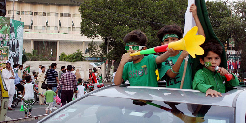 Children pop out of a cars sun roof with flags and horns.— PPI