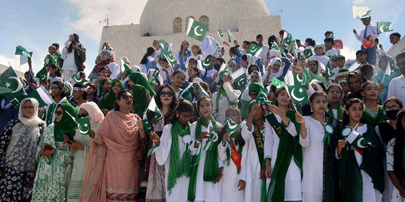 سکول کے بچے اپنے اساتذہ کے ساتھ مزار قائد پر 75 واں یوم آزادی منانے کے لیے پاکستانی پرچم لہرا رہے ہیں۔  - اے پی پی