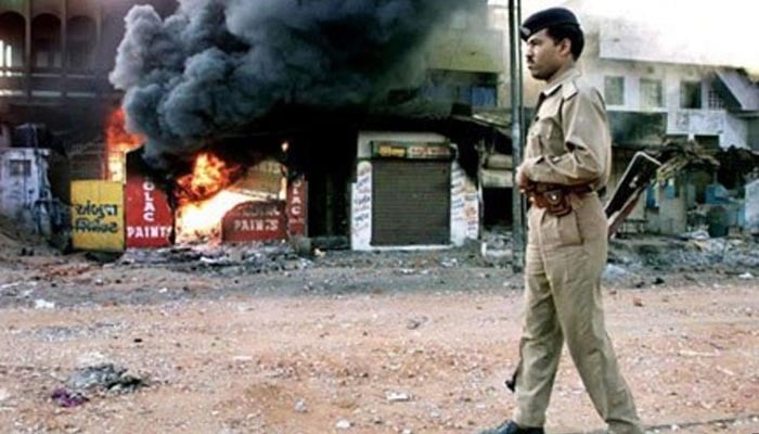 An Indian policeman stands on a street in Gujarat where shops can bee seen burnt releasing flames and smoke during the anti-Muslim riots in the state. — AFP/File