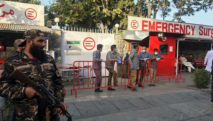 A Taliban fighter stands guard as Afghan medical staff members wait at the entrance of a hospital to receive the victims of an explosion in Kabul on October 3, 2021. PHOTO: AFP