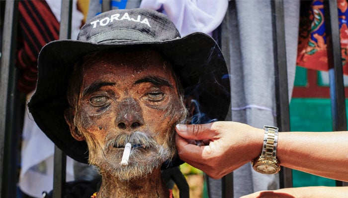 This picture taken on August 15, 2022 shows a family member performing the Manene traditional rite of cleaning the preserved remains of a deceased relative in Lembang. In a village on Indonesia´s Sulawesi island, residents pull coffins holding the preserved bodies of their loved ones from a burial cave carved into the mountainside in a ritual for the afterlife. — AFP