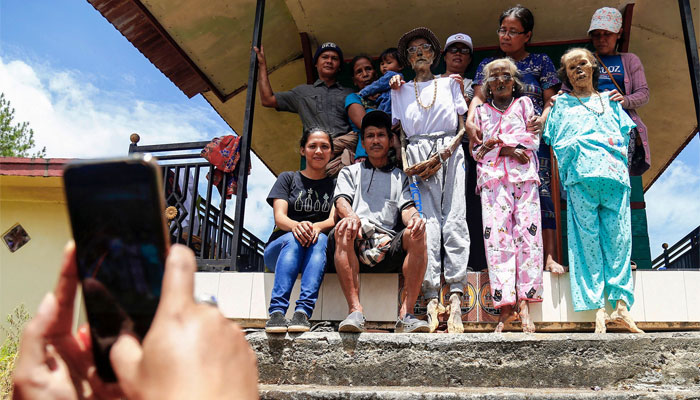 This picture taken on August 15, 2022 shows family members performing the Manene traditional rite of cleaning the preserved remains of deceased relatives in Lembang. In a village on Indonesia´s Sulawesi island, residents pull coffins holding the preserved bodies of their loved ones from a burial cave carved into the mountainside in a ritual for the afterlife. — AFP