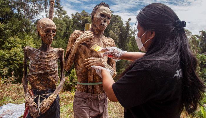 This picture taken on August 17, 2022 shows a family member of the Toraja ethnic group preparing the bodies of exhumed relatives from a community burial site to be cleaned and dressed in a series of traditional ceremonies honouring the dead known as Manene, in Torea village, in North Toraja, Indonesia´s South Sulawesi. In a village on Indonesia´s Sulawesi island, residents pull coffins holding the preserved bodies of their loved ones from a burial cave carved into the mountainside in a ritual for the afterlife. — AFP