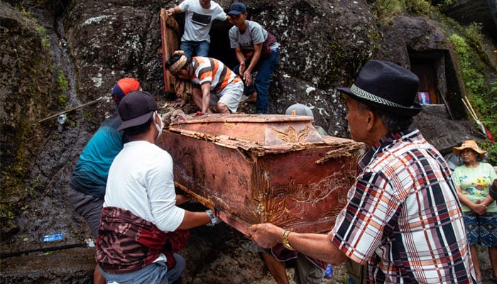 This picture taken on August 16, 2022 shows members of the Toraja ethnic group exhuming bodies of their relatives from a community burial site, to be cleaned and dressed in a series of traditional ceremonies honouring the dead known as Manene, in Torea village in North Toraja, Indonesia´s South Sulawesi. In a village on Indonesia´s Sulawesi island, residents pull coffins holding the preserved bodies of their loved ones from a burial cave carved into the mountainside in a ritual for the afterlife. — AFP