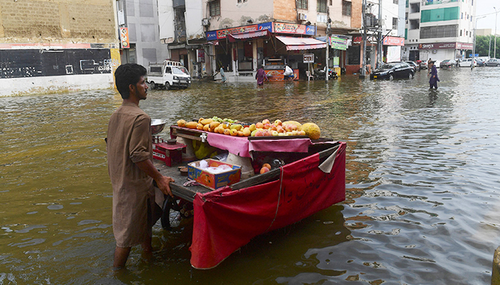 A fruit vendor pushes his cart across a flooded street following heavy monsoon rains in Karachi on July 26, 2022. — AFP