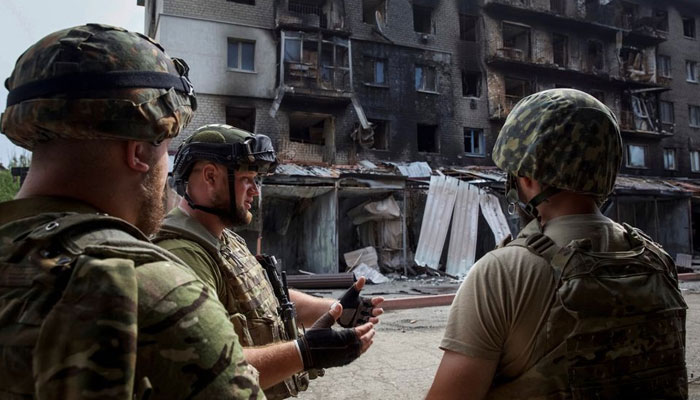 20 اگست 2022 کو یوکرین کے ڈونیٹسک کے علاقے سیورسک کے قصبے میں، یوکرین پر روس کے حملے کے دوران، یوکرائنی سروس کے ارکان روسی فوجی حملے سے تباہ ہونے والی رہائشی عمارت کے سامنے ایک دوسرے سے بات کر رہے ہیں۔ — رائٹرز