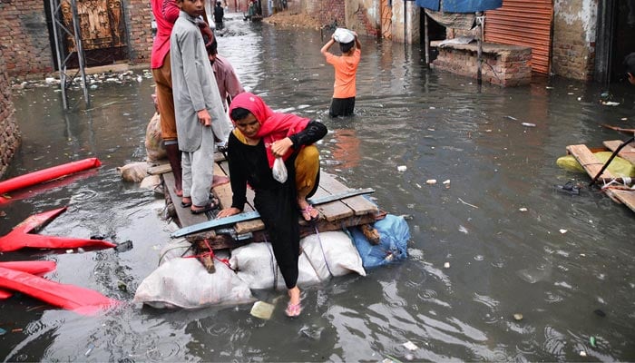 Rain affected people passing through rainwater on hand made boats after heavy rain in the city at Jinnah colony Latif Abad. — APP/File