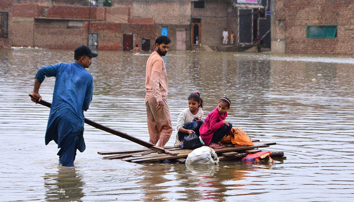 Rain affected residents use a wooden boat to float on the flood water in an area of Hyderabad. — APP