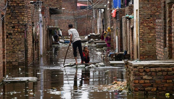 حیدرآباد، پاکستان میں 24 اگست، 2022 کو مون سون کے موسم کے دوران بارش کے بعد، ایک مرد اور ایک لڑکی سیلاب زدہ گلی کو عبور کرتے وقت عارضی بیڑا استعمال کر رہے ہیں۔— رائٹرز/فائل