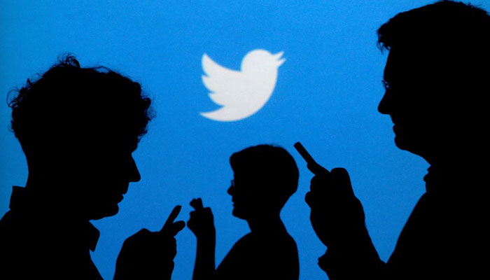 People holding mobile phones are silhouetted against a backdrop projected with the Twitter logo in this illustration picture taken September 27, 2013. — Reuters