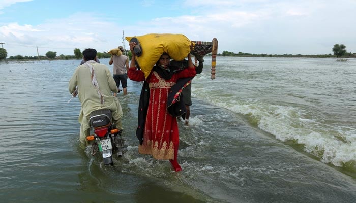 Stranded people carry their belongings as they wade through a flooded area after heavy monsoon rainfall in Rajanpur district of Punjab province on August 25, 2022. — AFP