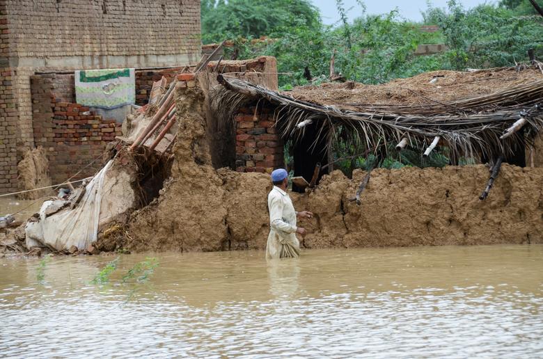 A man wades through flood waters beside his damaged house following rains and floods during the monsoon season in Dera Allah Yar, district Jafferabad, Balochistan, Pakistan August 25. — Reuters