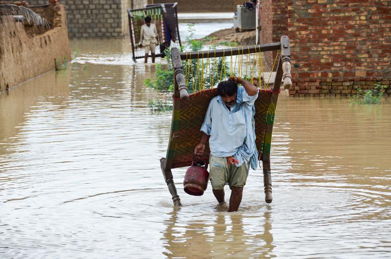 ڈیرہ اللہ یار، ضلع جعفرآباد، بلوچستان، پاکستان، 25 اگست کو مون سون کے موسم میں بارشوں اور سیلاب کے بعد مرد بارش کے پانی میں سے اپنا سامان لے کر چل رہے ہیں۔ — رائٹرز