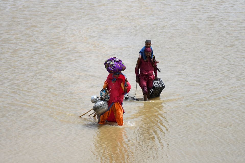 26 اگست 2022 کو پاکستان کے جامشورو میں مون سون کے موسم کے دوران بارشوں اور سیلاب کے بعد ایک خاندان اپنے سامان کے ساتھ بارش کے پانی میں بہہ رہا ہے۔ - رائٹرز