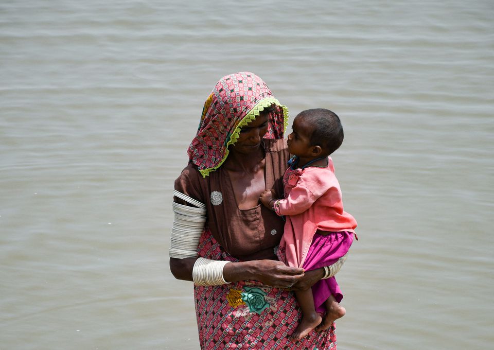 26 اگست 2022 کو پاکستان کے جامشورو میں مون سون کے موسم کے دوران بارشوں اور سیلاب کے بعد ایک خاتون اپنے بچے کو اٹھائے ہوئے بارش کے پانیوں سے گزر رہی ہے۔ — رائٹرز