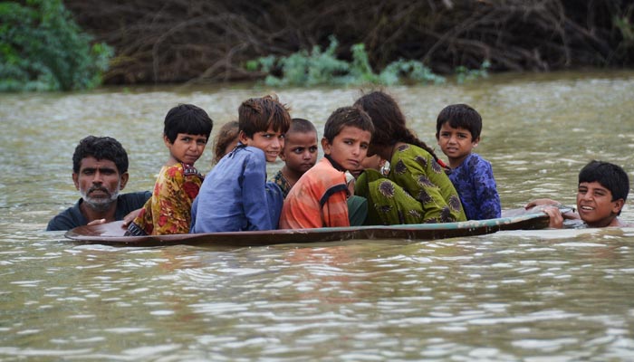 26 اگست 2022 کو صوبہ بلوچستان کے ضلع جعفرآباد میں مون سون کی شدید بارشوں کے بعد ایک شخص (L) ایک نوجوان کے ساتھ بچوں کو سیلاب زدہ علاقے میں منتقل کرنے کے لیے سیٹلائٹ ڈش کا استعمال کر رہا ہے۔ — AFP