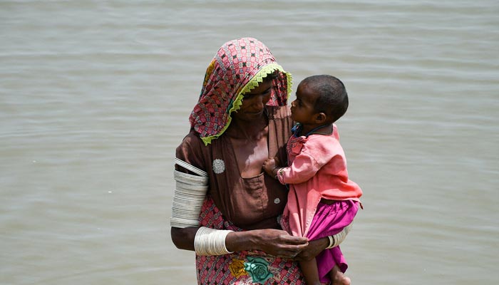 A woman carries her baby as she walks through rain waters following rains and floods during the monsoon season in Jamshoro on August 26, 2022.— Reuters